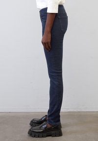 Hubené tmavě modré džíny s vysokým pasem, se klasickým pět pocket designem. Kombinované s černými masivními mokasínami.