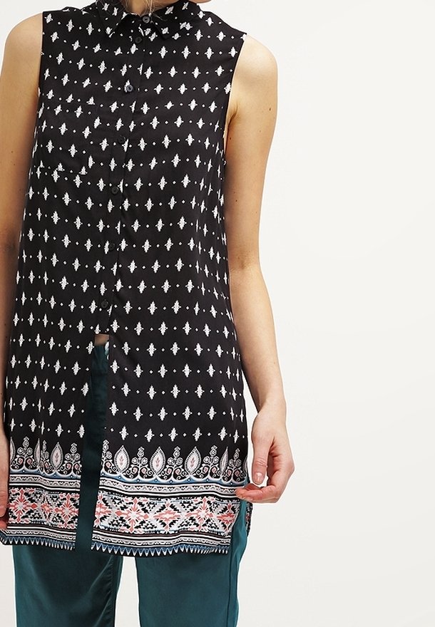 Czarna bluzka bez rękawów z zapięciem na guziki, zdobiona białymi geometrycznymi wzorami oraz dekoracyjnym brzegiem w stylu paisley w odcieniach różu i niebieskiego.