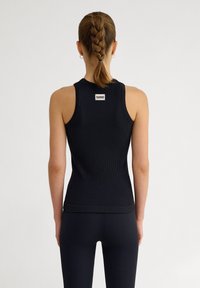 Top senza maniche nero a coste con collo tondo, caratterizzato da una piccola etichetta del logo sul retro. Il tessuto sembra morbido con un design aderente.