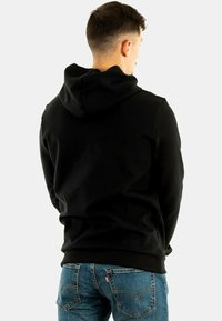 Sudadera con capucha negra y acabado texturizado, que presenta un bolsillo tipo canguro y puños de canalé, combinada con unos jeans de mezclilla azules.