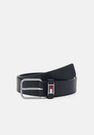 Cinturón de cuero azul marino con hebilla de metal plateado. Presenta una forma rectangular, textura suave y detalle de logo en rojo, blanco y azul.