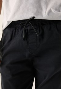 Black elastic-waist pants with a drawstring closure. Material appears smooth with a subtle sheen. Features pockets and a relaxed fit.