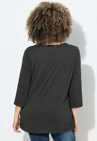 Zwart en goud gestreepte langarmtop met een ronde hals en een losse pasvorm, gemaakt van een zacht materiaal, gecombineerd met blauwe jeans.