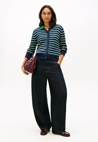 Ζακέτα με ναυτικά ριγέ και πράσινο γιακά, κουμπωτή μπροστά· συνδυασμένη με παντελόνι πλατύ στο πόδι από σκούρο τζιν και μπορντό τσάντα.