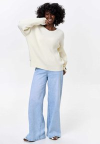 Cream ribbed knit sweater with long sleeves paired with light blue wide-leg jeans. Notable detail: button accents on the sweater sleeves.