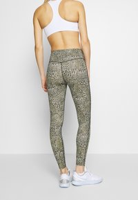 Leggings a stampa leopardata con vita alta, realizzati in tessuto elastico, con una texture morbida e dettagli lungo i lati. Sneakers bianche.