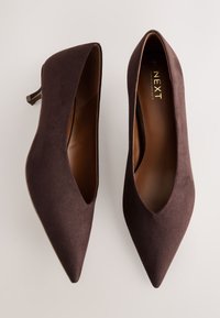 Paire d'escarpins marron en daim à bout pointu avec petits talons fins, vue de dessus sur fond clair.
