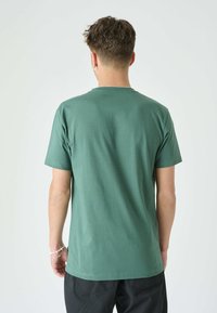 Grünes Baumwoll-T-Shirt mit rundem Ausschnitt und kurzen Ärmeln. Glatte Textur, schlichtes Design und keine sichtbaren Muster oder Akzente.
