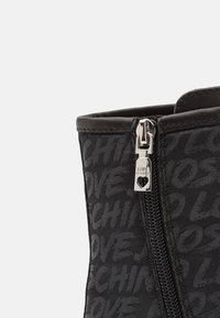 Bottines noires avec un tissu texturé sur lequel sont imprimés les motifs "LOVE" et "CHINOS". Fermeture éclair sur le côté avec une tirette en forme de cœur. Détails en cuir lisse.