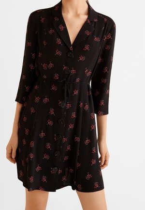 Czarna sukienka zapinana na guziki z rękawami do połowy przedramienia, paskiem w talii i rozmieszczonymi drobnymi czerwonymi kwiatowymi wzorami na tkaninie.