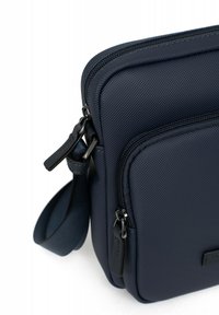 Borsa a tracolla navy in tessuto testurizzato, con scomparti con zip e dettagli in metallo nero. Forma rettangolare compatta con tracolla regolabile.