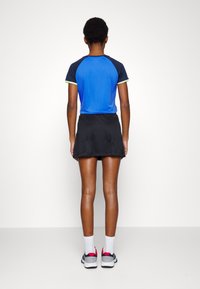 Conjunto deportivo azul y negro que incluye una camiseta azul de manga corta con detalles verdes y una falda negra. Se lleva con calcetines blancos y zapatillas deportivas.