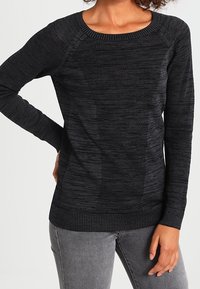 Černý svetr s dlouhými rukávy, texturovanými ribkovými a hladkými pletenými vzory, kulatým výstřihem a volným střihem, spárovaný se šedými kalhotami.