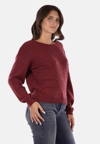 Maglione bordeaux con collo a giro, maniche lunghe e polsini a coste. Realizzato in un tessuto a maglia testurizzato, presenta delicate decorazioni sparse.