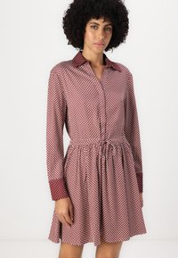 Rochie cu buline roșii și albe, cu guler, mâneci lungi și talie strânsă; material ușor; model jucăuș; lungime deasupra genunchiului.