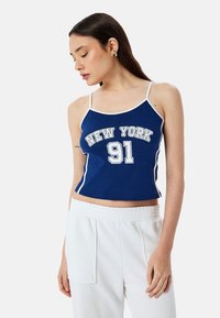 Blauwe crop top met witte afwerking waarop "NEW YORK" en "91" in vet afgerukte lettertype staan. Het materiaal lijkt zacht en goed aansluitend.