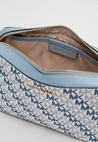 Pochette con rifiniture in pelle blu, caratterizzata da un motivo geometrico bianco e blu. Hardware in tonalità oro e interno foderato con etichetta. Chiusura con zip.