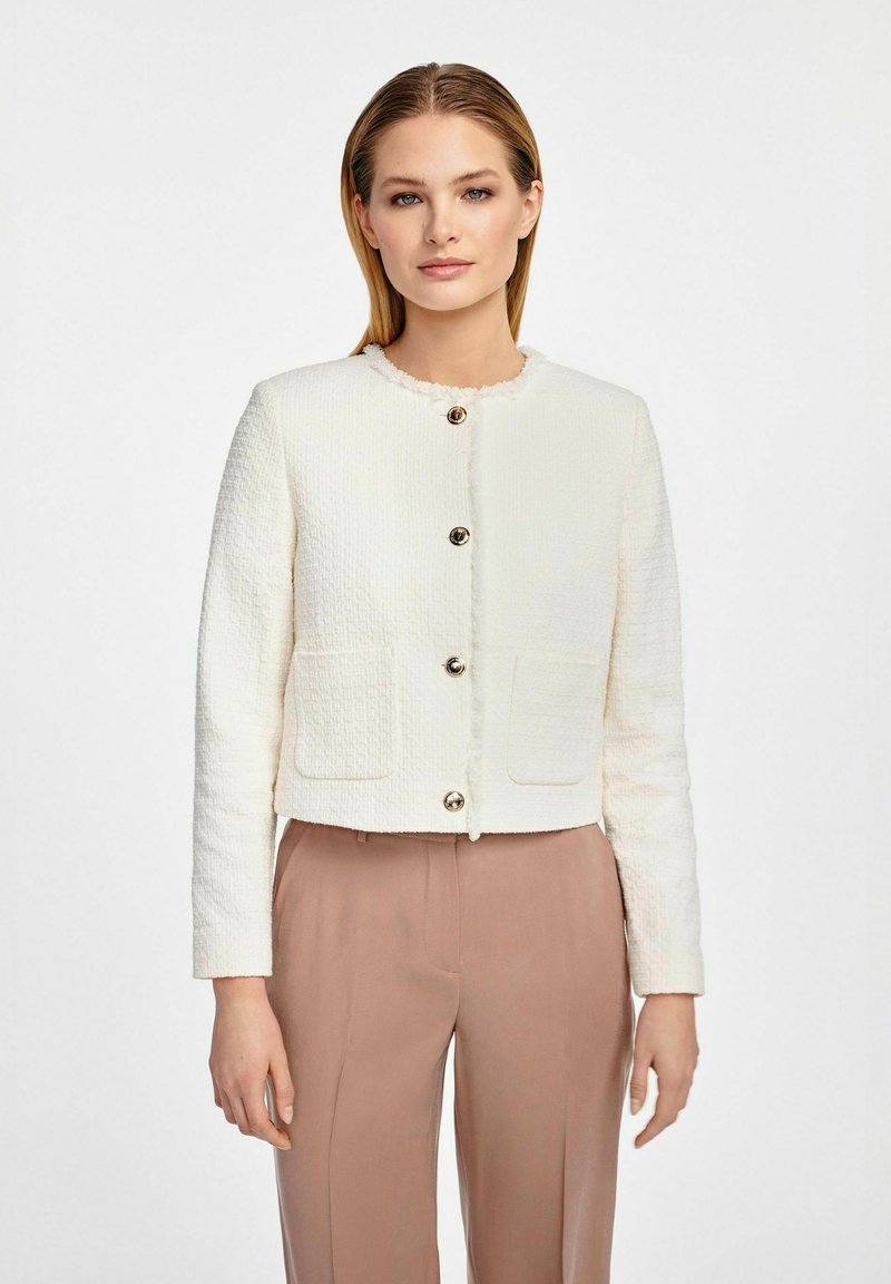 Biała, fakturowana krótka kurtka z okrągłym dekoltem, zapięcia na srebrne guziki i dwiema przednimi kieszeniami, zestawiona z jasnoróżowymi spodniami.