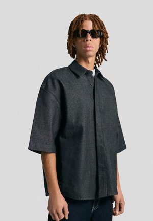Korte mouwen, donkergrijze knoopshirt gemaakt van gestructureerde stof; heeft een klassieke kraag en een ontspannen pasvorm met zichtbare stikseldetails.