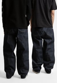 Jeans in denim di un blu scuro indaco, con una vestibilità ampia, gambe dritte, cuciture sottili lungo le tasche e bordi consumati vicino all'orlo.