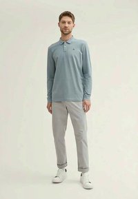 Vaaleansininen pitkähihainen poolopaita, jossa on kaulus ja kolmen napin aukko, yhdistettynä vaaleanharmaisiin, käärityihin chinopöksiin ja valkoisiin tennareihin.