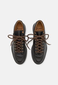 Chaussures en cuir noir avec une texture granuleuse, lacets marron et œillets en métal. Avec une pointe arrondie et un design de semelle plate.