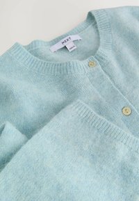Lichtblauwe cardigan van zacht breiwerk, met een ronde halslijn, geribbelde manchetten en twee kleine gele knopen aan de voorkant.