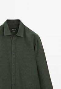 Dark green button-up shirt made of textured fabric; features a classic collar and six buttons down the front. Brand label visible.
