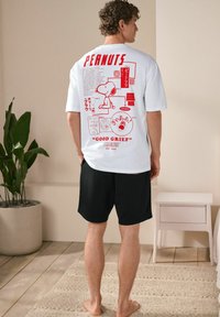 White t-shirt with red graphic design featuring Snoopy and text, paired with black shorts. Casual fit, cotton material, shown from the back.