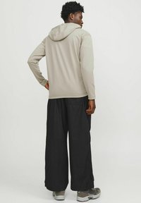 Light grey hooded sweatshirt with long sleeves, paired with loose black trousers. The outfit features a smooth texture and relaxed fit.