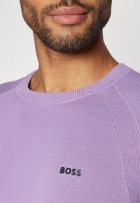 Levandų megztinis su raukšlėtu apykakle ir tekstūruotais detalėmis ant rankovių, su juodu "BOSS" logotipu ant krūtinės.