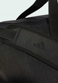 Black duffel bag featuring a textured fabric, thick straps, and a subtle logo. The design emphasizes functionality and durable materials.
