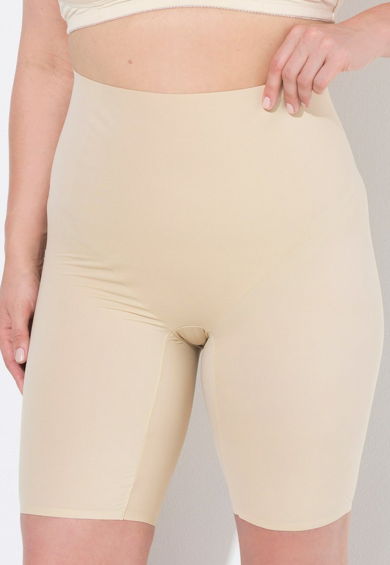 Pantaloncini modellanti beige a vita alta con una texture liscia e elasticizzata, di lunghezza a metà coscia. Presentano un design senza cuciture e cuciture minime.