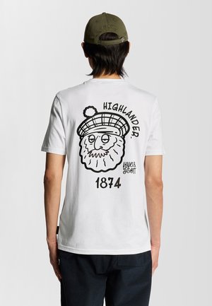 T-shirt bianca in cotone con una grafica nera sul retro che raffigura un personaggio barbuto con un cappello a scacchi, accompagnato dal testo "HIGHLANDER" e "1874."