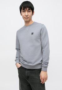 Grå genser med rund hals, ribbestrikkede mansjetter og en liten logo på brystet. Materialet virker mykt og lett teksturert.