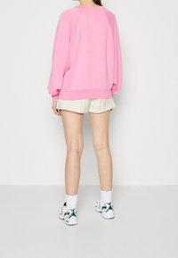 Różowa bluza oversize z prążkowanym wykończeniem na dole, zestawiona z jasnobeżowymi szortami. Całość dopełniają białe trampki z zielonymi akcentami.