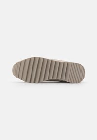 Sola do sapato com uma superfície de borracha beige texturizada, com ranhuras horizontais para tração e um bico arredondado.