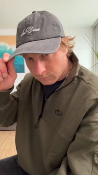 Căciulă de baseball gri cu "Les Deux" brodat în alb. Persoana poartă o jachetă din fleece de culoare verde măsliniu închis, cu guler cu fermoar. Fundal neutru.