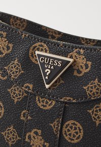 Fekete textúrájú kézi táska barna logó mintával, arany háromszög alakú logóval, amelyen az áll: "GUESS USA." Varrott részletek láthatók.