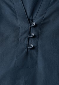 Maglietta blu navy con scollo a V, tre bottoni scuri e tessuto dalla texture morbida, con orlo pulito e dettagli di cucitura sottili.