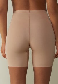 Beige rekbare shorts met een zachte textuur, tot halverwege de dij, en een naadloos ontwerp. Subtiele stiksels langs de randen. Geen zichtbare print.