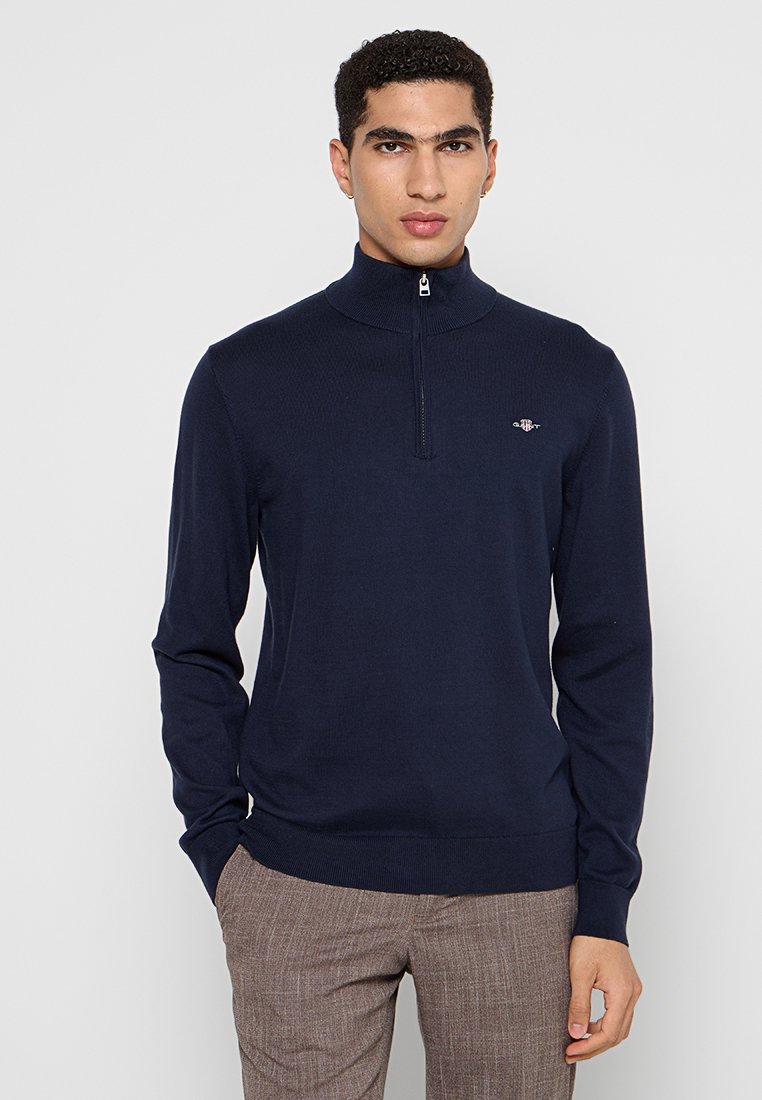 Granatowy sweter zapinany na zamek, wykonany z teksturowanej dzianiny, z wysokim kołnierzem i małym haftowanym logo na piersi. Dopasowany krój.