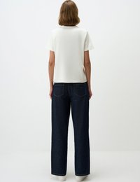Weißes kurzärmliges Oberteil kombiniert mit hochgeschnittenen, dunklen Jeans aus Denim mit geradem Schnitt und minimalistischem Design, das einen sauberen Abschluss bietet.