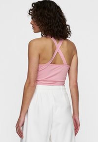 Top deportivo rosa con un cuerpo ajustado, tirantes cruzados en la espalda y textura suave, combinado con pantalones blancos de cintura elástica.