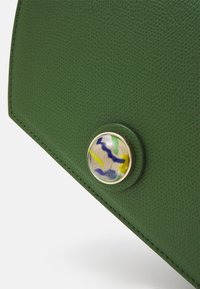 Zelená kožená kabelka v rohu s texturovaným povrchem, vybavená kulatým uzavíráním s vícemořádným designem v zlatém rámečku.