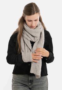 Lichtgrijze gebreide sjaal met een gestructureerd patroon, losjes om de nek gewikkeld, met ribbelaccenten aan de uiteinden, gedragen met een zwarte shirt.