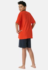 Orange short-sleeve T-shirt with relaxed fit, paired with navy blue shorts. Fabric appears soft, minimal design, no visible patterns or accents.