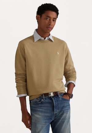 Beige lange mouw trui met een ronde hals, gedragen over een lichtblauw gestreept shirt, gecombineerd met blauwe jeans en een bruine riem.
