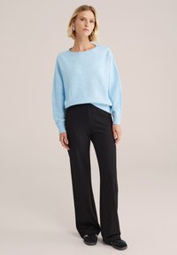 Lichtblauwe gebreide trui met geribde boorden, gecombineerd met zwarte pinstripebroeken. De look wordt afgemaakt met zwarte sneakers.