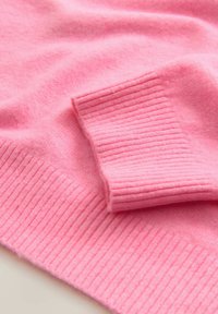 Suéter rosa de punto con puños y dobladillo acanalados, textura suave y acabado liso, destacando su color y diseño uniformes.